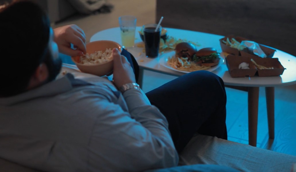 Guy seating on the couch, eating popcorns, watching tv